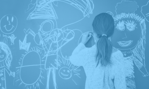 Teenage girl doodling on a chalkboard images of people, smiley faces arrows and other shapes. She is facing away from the camera and her hair is tied back in a low ponytail.