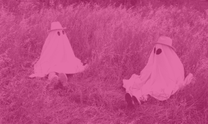 Two people dressed up as ghosts sitting on the grass